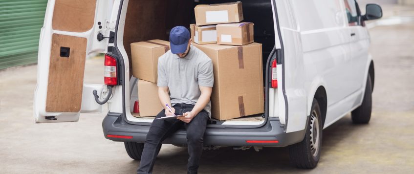 Delivery man writing on clipboard while sitting on the cargo area of his van