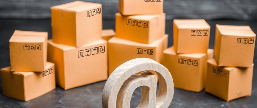 Wooden email symbol on the background of a variety of boxes. Warehouse of goods, online store, sale of goods through the Internet. Online sales and e-commerce, product and brand promotion.